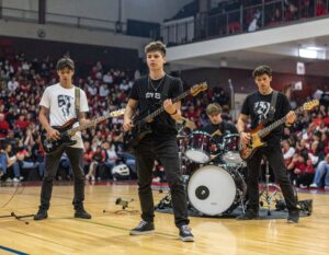 A high school rock band performing at a high school pep rally in the gym. 