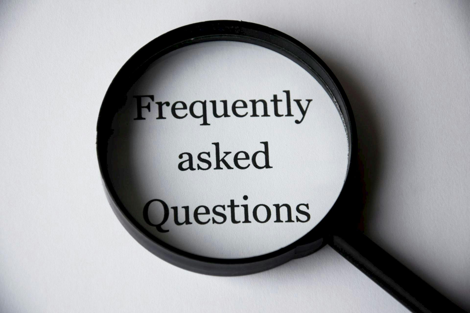 A photo of a black magnifying glass laying over the words "Frequently asked questions" on a white background